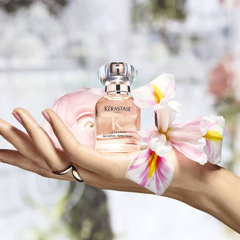 יד אוחזת בבושם לשיער Le Parfum על רקע פרחוני